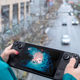 A person plays the Valve Steam Deck while looking out over a busy road.